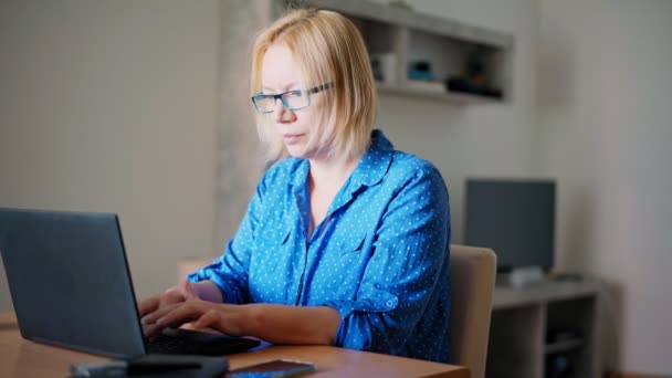 Vuxen blond kvinna som arbetar på en bärbar dator hemma. — Stockvideo