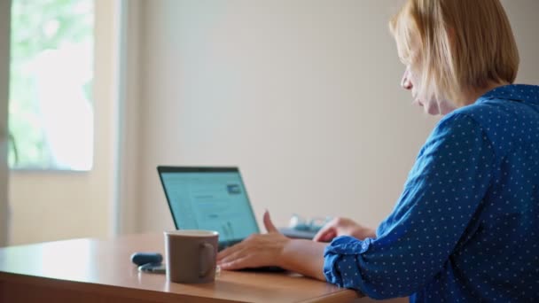 Задняя фотография белокурой молодой женщины, смотрящей на экран ноутбука во время работы — стоковое видео