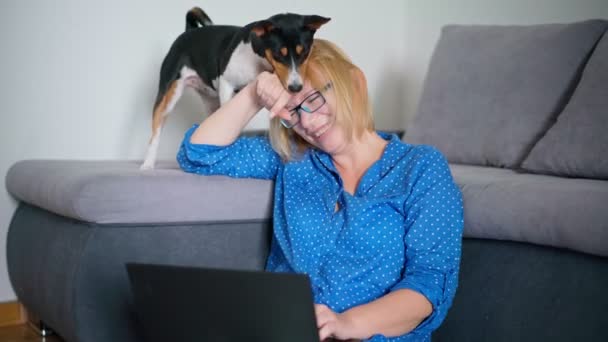 O femeie care lucrează pe un laptop în timp ce stă pe podea cu câinele ei drăguț — Videoclip de stoc
