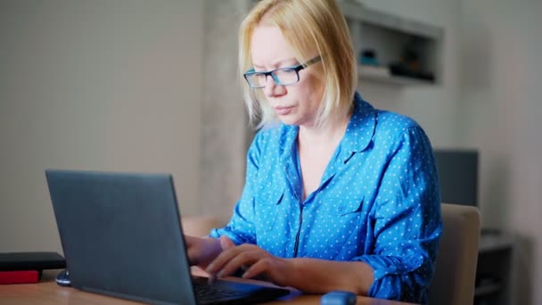Mujer rubia adulta trabajando en un portátil en casa. — Vídeos de Stock