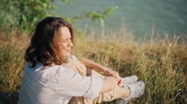 Tepedeki kuru çimlerde oturan ve manzaraya bakan genç bir kadın.