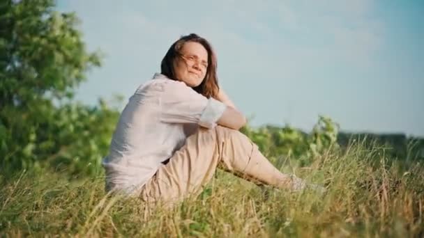 A young woman sitting at the dry grass on the hill and enjoying the view — Stock Video