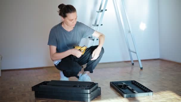 Professional repairwoman with tool belt assembles a plastic shelf from parts — Stock Video