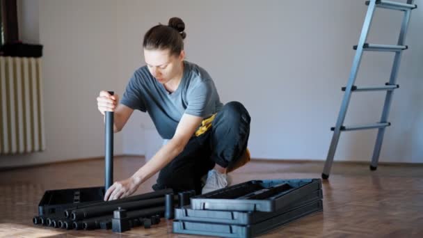 Professional repairwoman with tool belt assembles a plastic shelf from parts — Stock Video