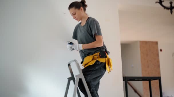Una reparadora profesional desenrosca un perno de la pared con un destornillador — Vídeos de Stock