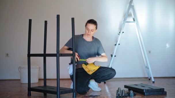 A professional repairwoman with a tool belt measures a plastic shelf — Stok Video