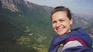 Neşeli genç bir kadın seyahati sırasında dağların arka planında selfie çekiyor.