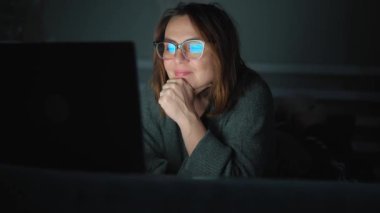 Yetişkin bir internet bağımlısı kadın gece geç saatlerde dizüstü bilgisayarla yatakta yoğunlaşıyor.