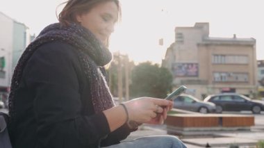 Güzel bir yetişkin kadının portresi. Elinde telefonlar, sıcak bir sonbahar gününde Avrupa 'da bir bankta oturuyor.