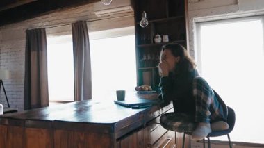 Sabahları pijamalı uykulu bir kadın mutfakta oturuyor, esniyor ve dizüstü bilgisayarla çalışmaya başlıyor..