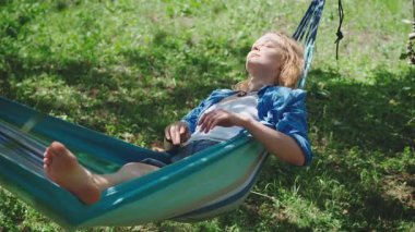Güneşli bir yaz gününde hamakta dinlenen uzun saçlı güzel bir genç kadın. Boş zaman, özgürlük ve kaygısız yaşam tarzı konsepti sıcak doğal ışıkta.
