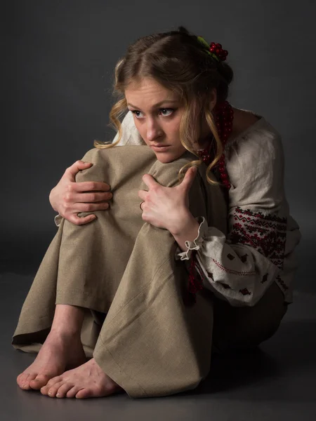 Pretty poor frightened girl  in Ukrainian embroidery  sitting on the floor — Stock Photo, Image