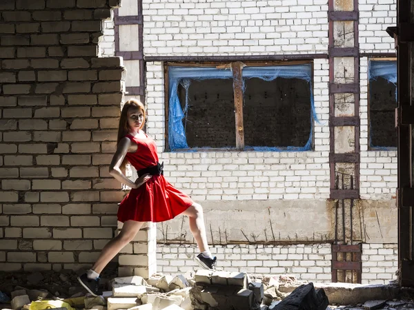 Рыжая тонкая стройная девушка с веснушками в красном платье на фоне стены разрушенного здания — стоковое фото