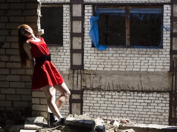 Рыжая тонкая стройная девушка с веснушками в красном платье на фоне стены разрушенного здания — стоковое фото