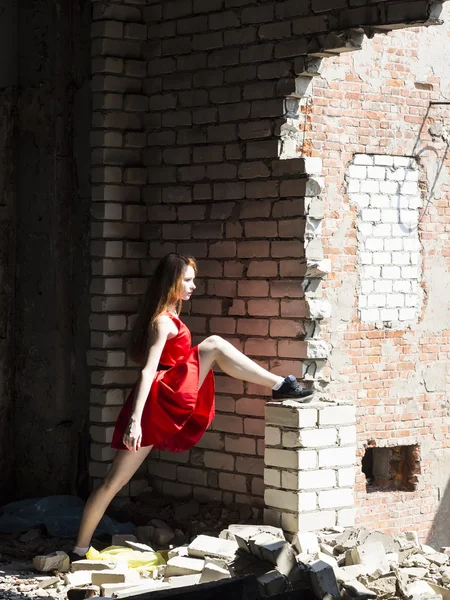 Vörös hajú vékony karcsú lány piros ruhás, háttérben a fal elpusztult épület szeplőkkel — Stock Fotó