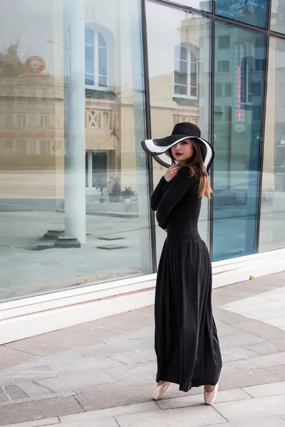 Танцовщица в шляпе и пуантах в красивом темно-сером платье на фоне окна. Классика, современность, современность — стоковое фото