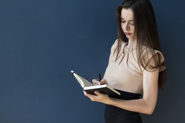 Sekreter bir defter mavi bir arka plan üzerinde notlar yapar. İş kadını