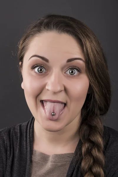 La chica muestra la lengua sobre un fondo gris. Emociones, piercings — Foto de Stock