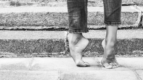 Barfota dansare fot i jeans och en fot på bakgrunden av stentrappor. Sexiga kvinnliga ben. Svartvitt foto — Stockfoto