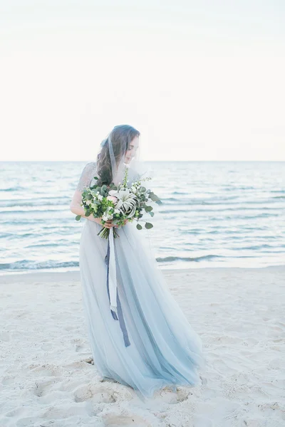 Tenera sposa in velo con bouquet da sposa al mare — Foto Stock