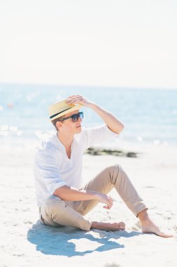 İyi görünümlü bir adam deniz kıyısı oturan şapkalı