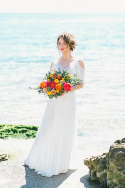 Genç gelin düğün buket deniz kenarında tutarak