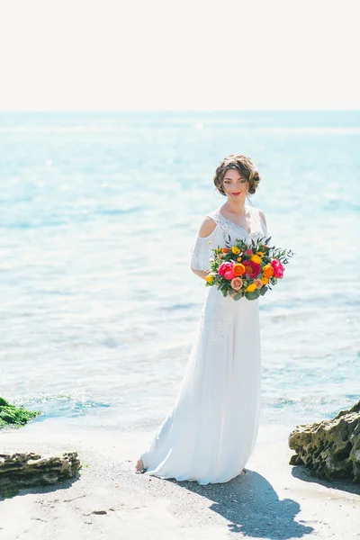 Giovane sposa tenendo bouquet da sposa in riva al mare — Foto Stock