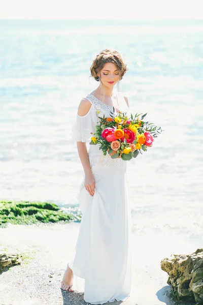 Jovem noiva segurando buquê de casamento pelo mar — Fotografia de Stock