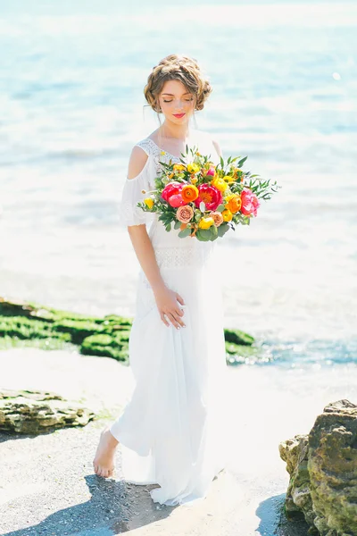 Giovane sposa tenendo bouquet da sposa in riva al mare — Foto Stock