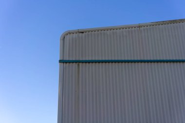 Açık mavi gökyüzünün altında bükülmüş metalle sanayi binasının köşesi..