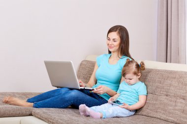 Anne ile bir dizüstü bilgisayar, telefon kanepede kızıyla.