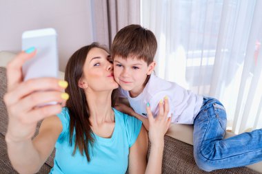  Young mother and her son taking a selfie on the sofa.Happy fami clipart