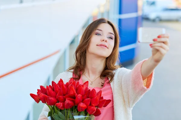 Jovem loira com um buquê de tulipas vermelhas está tomando selfie — Fotografia de Stock