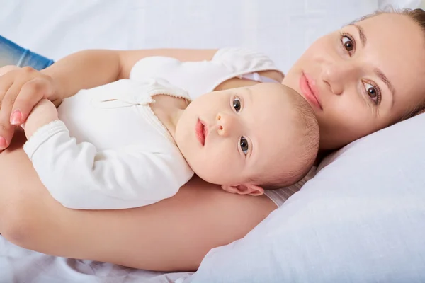 Madre con el bebé en sus brazos en la cama, mirando hacia arriba y sonriendo . — Foto de Stock