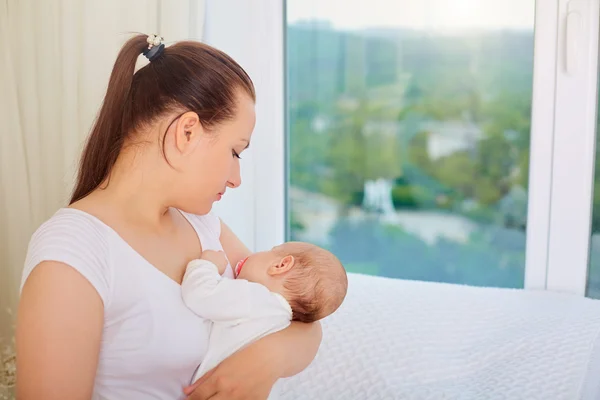 Mother with a sleeping baby in her arms at the window. — Stock Photo, Image