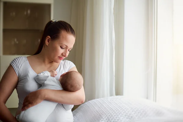 Happy young mother and her baby at window at bright sunny day. — Stock Photo, Image