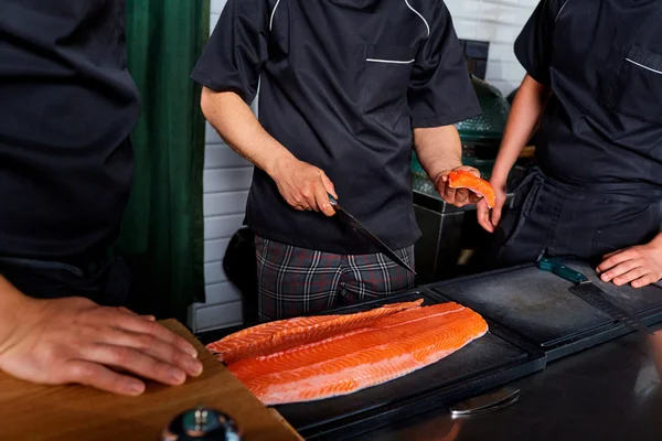 Three chefs cooks in uniform cutting salmon fish on fillets with — Stock Photo, Image