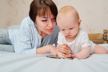Anne ve bebek yatakta telefonla oynuyorlar. Annem bakıyor.