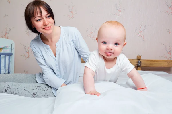 Bebé con la lengua colgando en una cama en una habitación con la madre —  Fotos de Stock