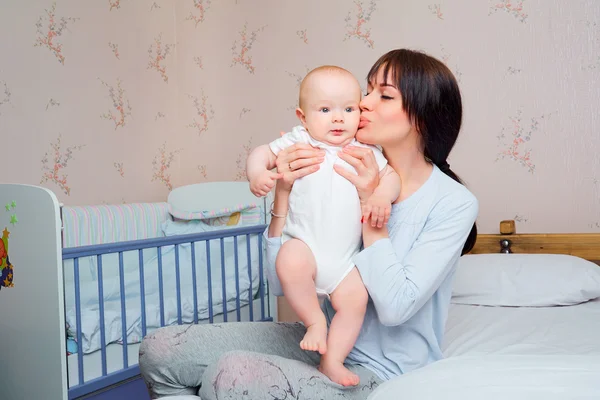 Mamá pijama tiernamente besa al niño en la cama en la habitación . — Foto de Stock