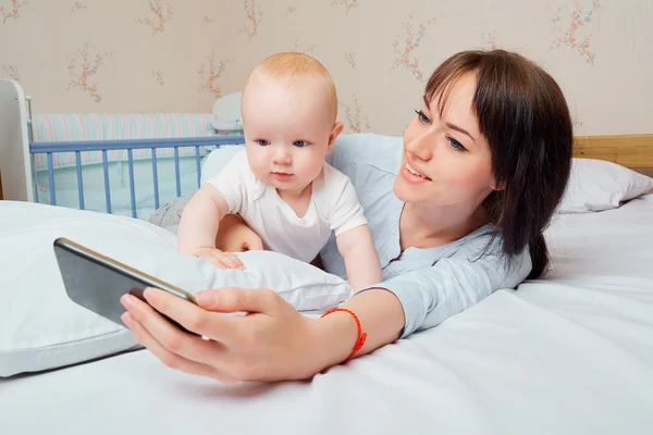 Maman et bébé avec le téléphone sur le lit dans la chambre . — Photo