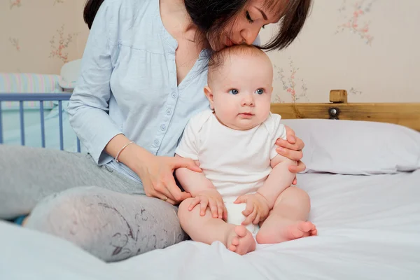 母親はベッドの上で赤ん坊を抱きしめ、子供にキスをした。幸せな家族 — ストック写真