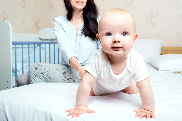 Bébé avec sourire traînant sur un lit dans une chambre avec mère. L ' — Photo