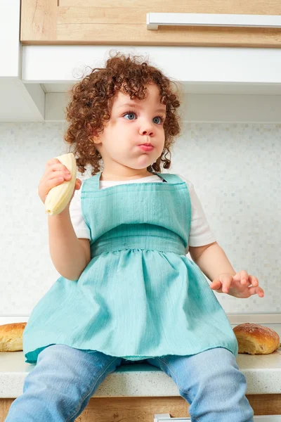 A child on the kitchen table. Funny little, curly girl sitting o