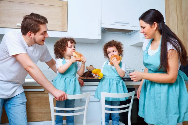 Jumelles fille avec ses parents dans la cuisine manger des petits pains. Un heureux — Photo