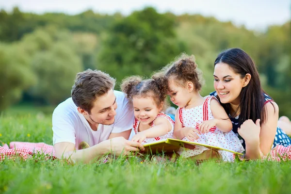 Mladá rodina s knihou venku ležící na trávě v p — Stock fotografie