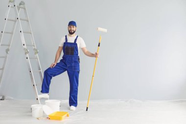 Gülümseyen işçi ressam dairede boya silindiriyle dikilip tamir için kameraya bakıyor.