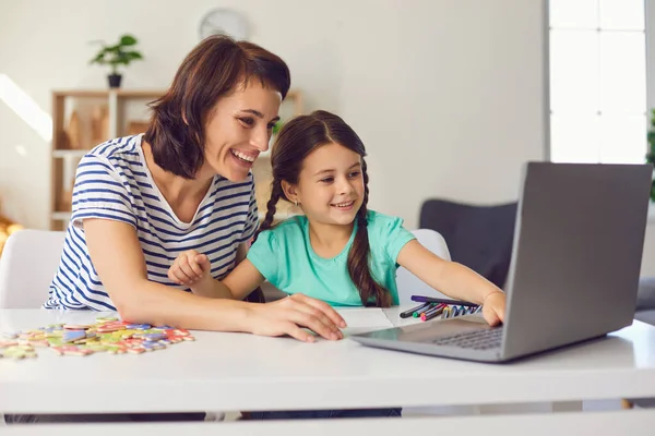 Moeder en haar dochtertje lachen terwijl ze een video op een laptop kijken terwijl ze aan een tafel zitten. — Stockfoto