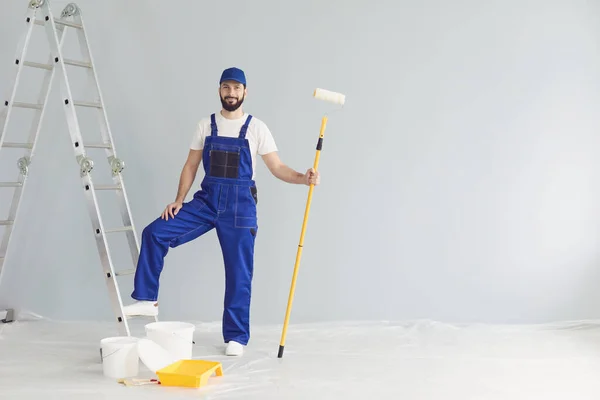 Lächelnder Arbeiter-Maler steht mit Farbroller zur Reparatur in Wohnung und blickt in Kamera — Stockfoto