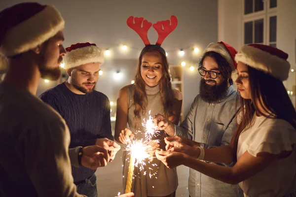Group of young male and female friends stand in a circle and light sparklers on New Years Eve. — Stock Photo, Image